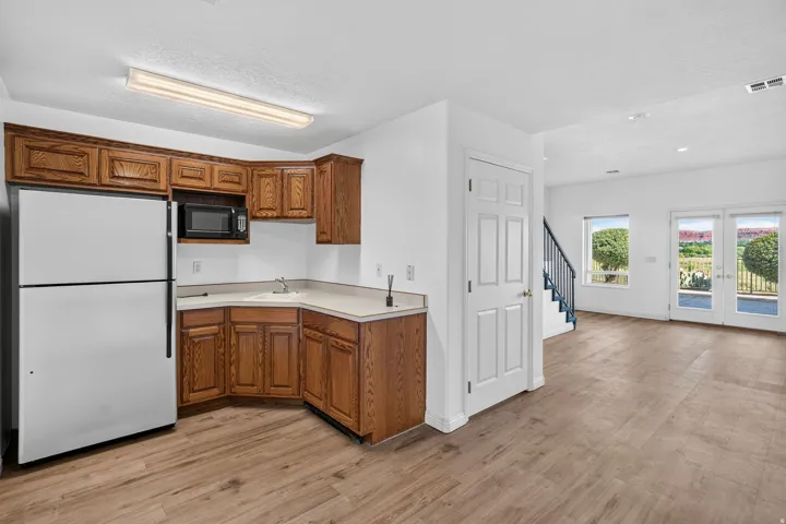 Open-concept living area with wood-finish flooring throughout, featuring a compact kitchenette with wood cabinetry, white appliances, and stainless steel sink