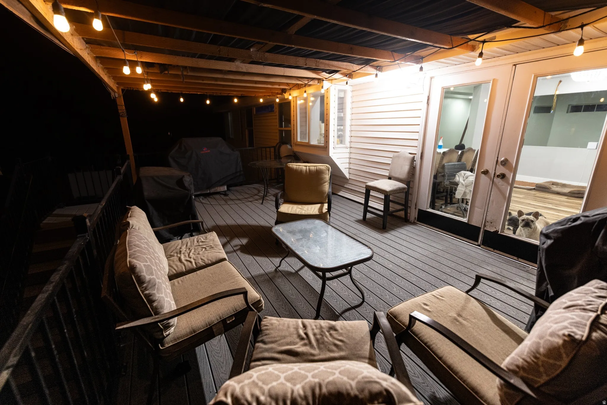 Outdoor deck with wood-finish flooring, featuring a covered patio area with exposed wood beams and string lighting