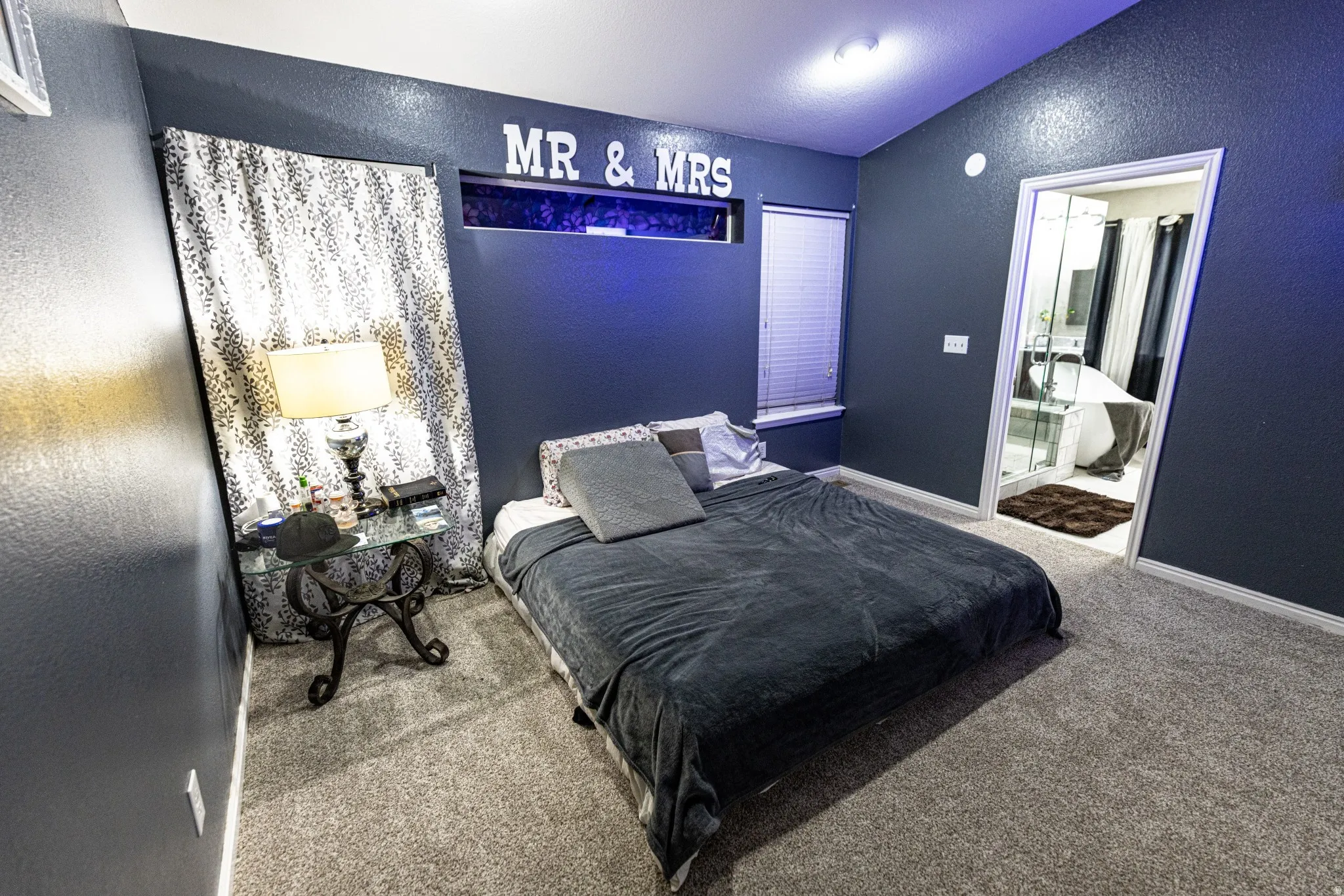 Carpeted room with a window featuring blinds, an entryway, and a permanent wall-mounted decorative element