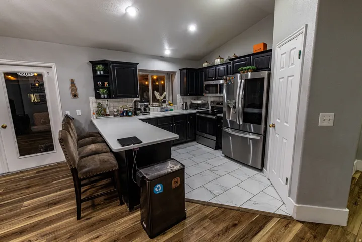 Kitchen featuring black cabinetry, stainless steel appliances, a white tile backsplash, and a breakfast bar with a light-toned countertop