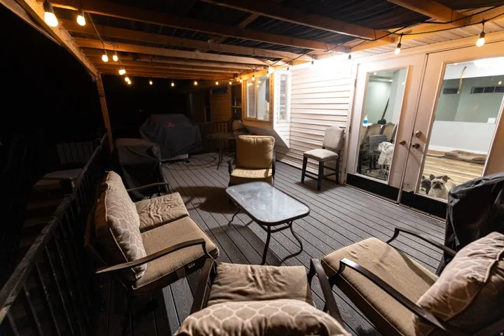 Outdoor deck with wood-finish flooring, featuring a covered patio area with exposed wood beams and string lighting