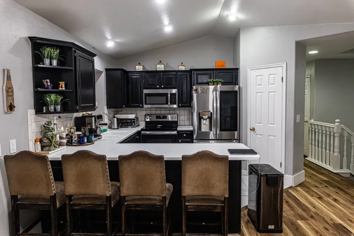 Kitchen featuring a white countertop, black cabinetry, stainless steel appliances, and a tile backsplash