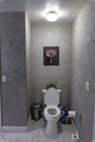 Textured wall finish, flush mount lighting fixture, white porcelain toilet, and large format floor tiling