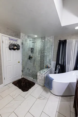 Walk-in shower with glass enclosure, freestanding soaking tub, tiled flooring, built-in shower bench, and recessed lighting