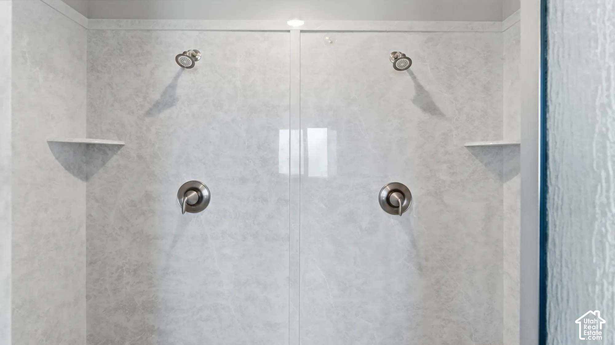 Dual shower heads with brushed nickel finishes, integrated wall shelving, and a clear glass enclosure