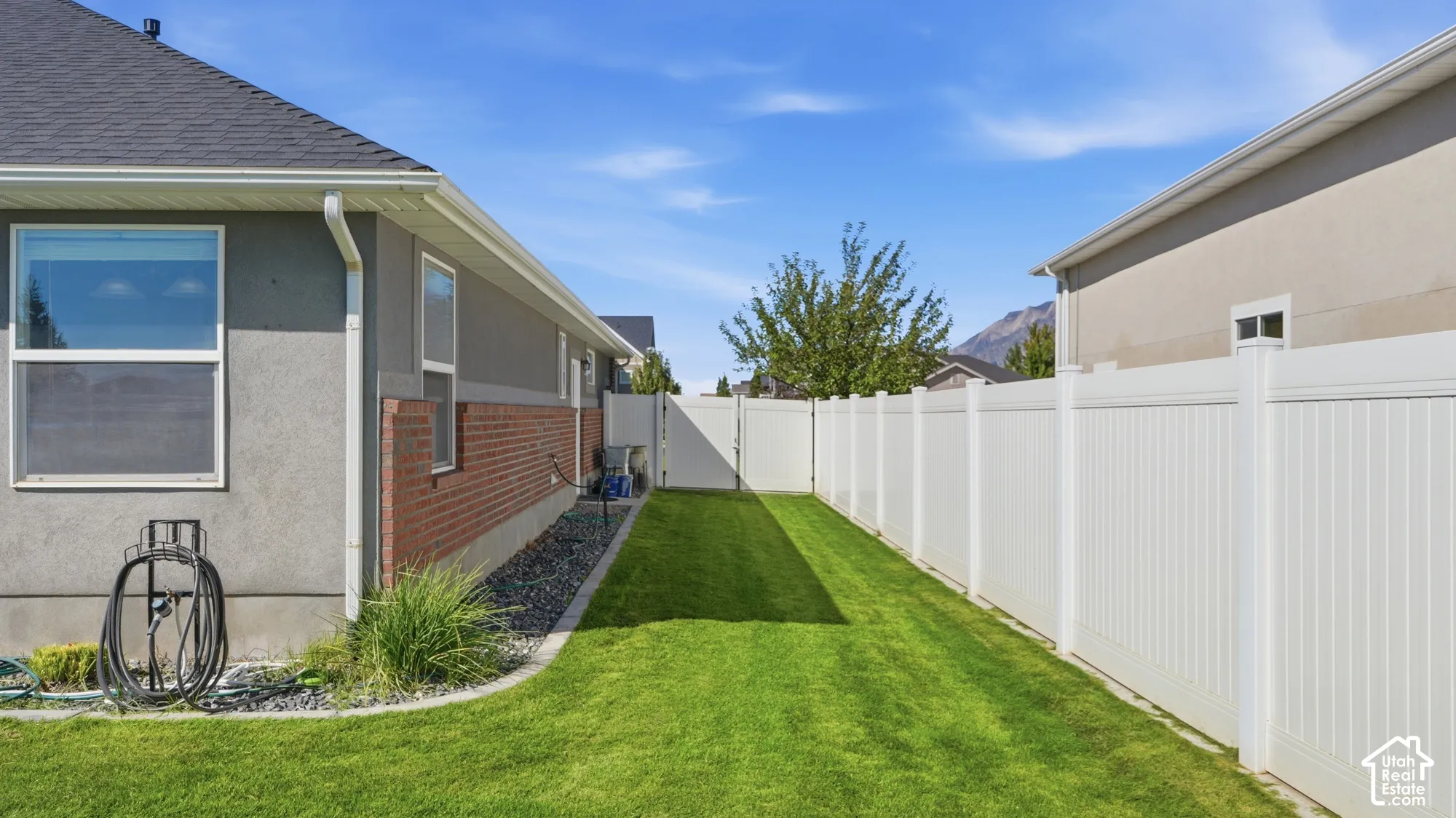 Exterior showcasing a gray stucco and brick facade with a dark shingle roof, accompanied by a white privacy fence and a manicured lawn
