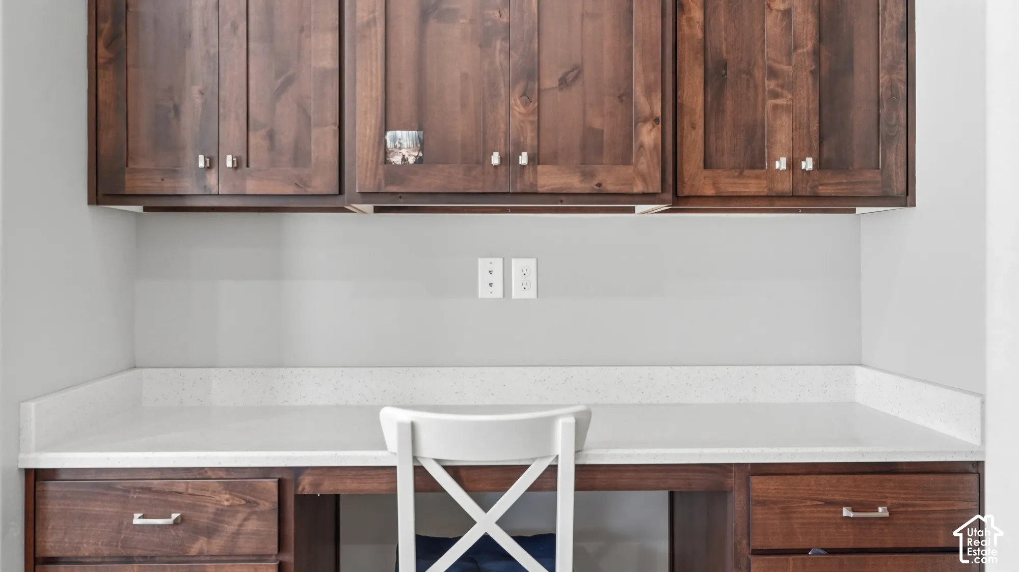 Built-in desk with wood-finish cabinetry, light-toned countertop, and overhead storage