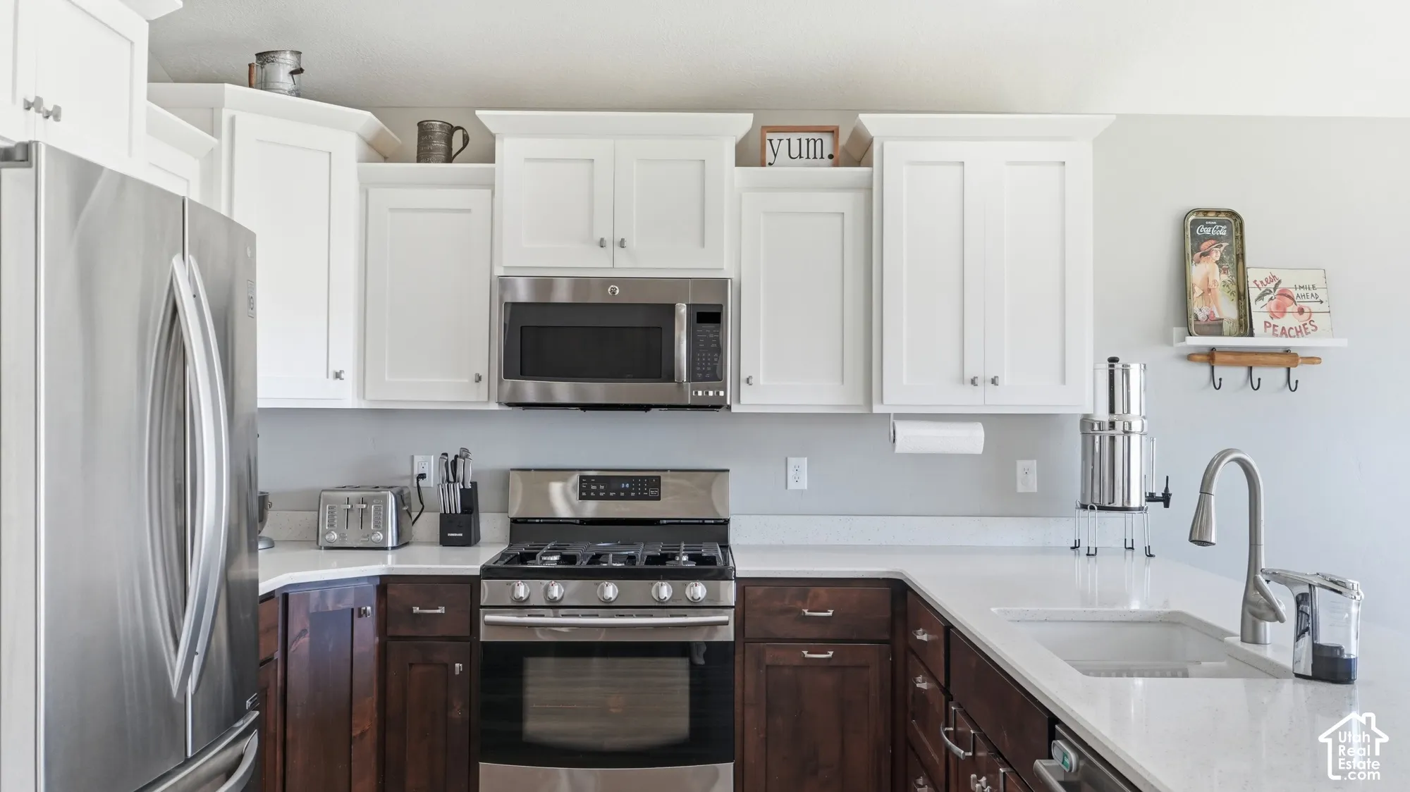 Kitchen featuring white upper cabinetry, dark wood-finish lower cabinetry, light-toned countertops, stainless steel appliances, and a stainless steel sink with a pull-down faucet