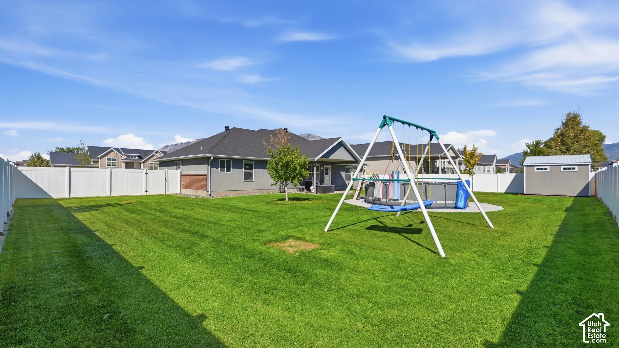 Expansive backyard with a manicured lawn, white privacy fencing, and a detached storage shed
