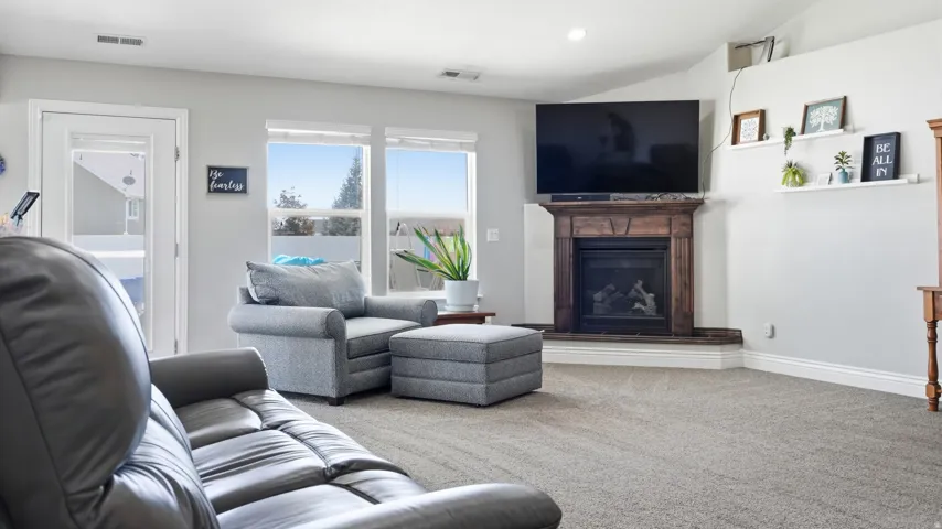 Vaulted ceiling, corner fireplace with wood mantle, carpeted flooring, large windows, and a glass-paneled door