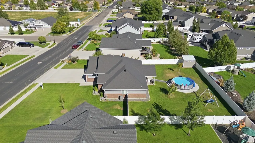 Expansive green lawn, white privacy fencing, paved driveway, mature trees, and a storage shed