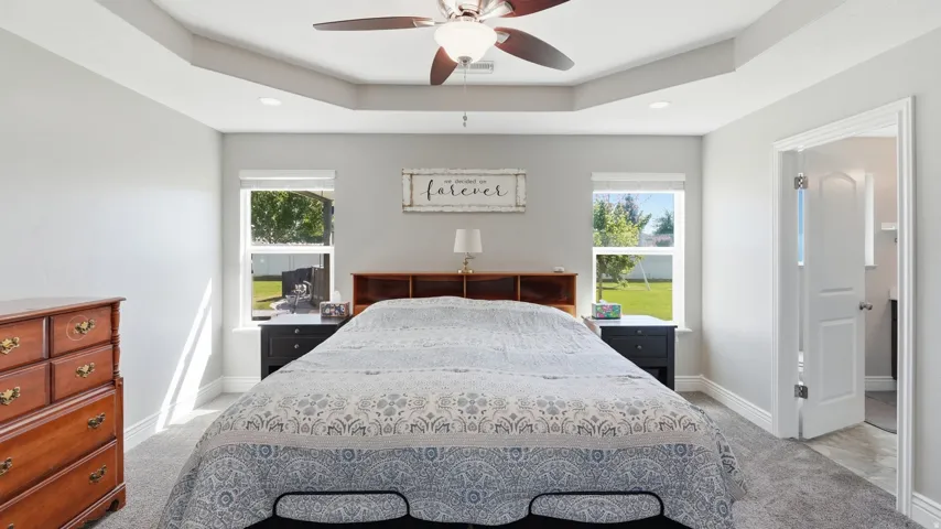 Tray ceiling with recessed lighting and a ceiling fan, dual windows, and carpet flooring