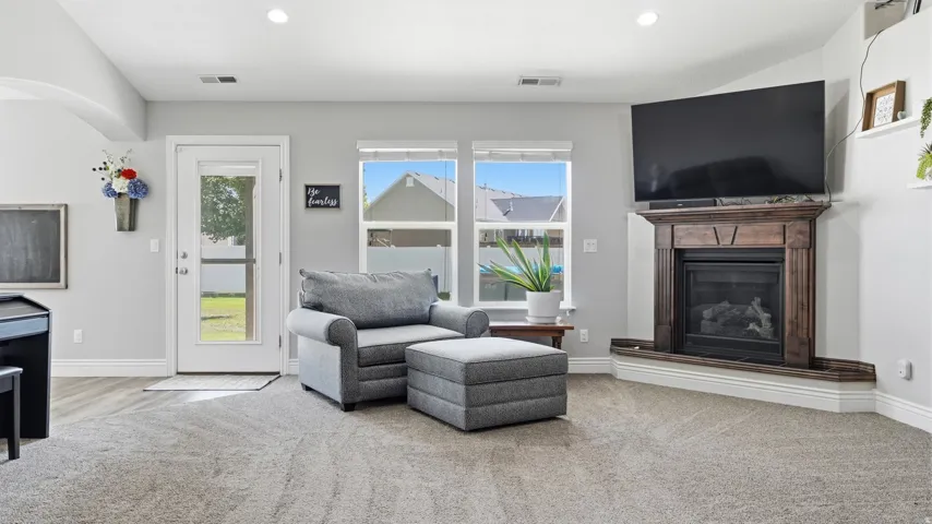 Living area featuring a corner-mounted fireplace with a wood-finish mantel, recessed lighting, and light-toned carpeting