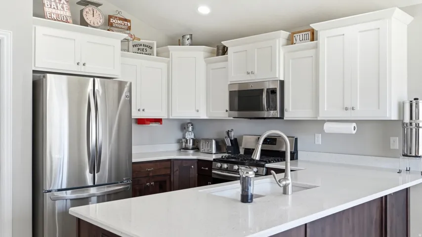Stainless steel appliances, white cabinetry, dark wood base cabinets, light-toned countertops, and a kitchen island with an undermount sink