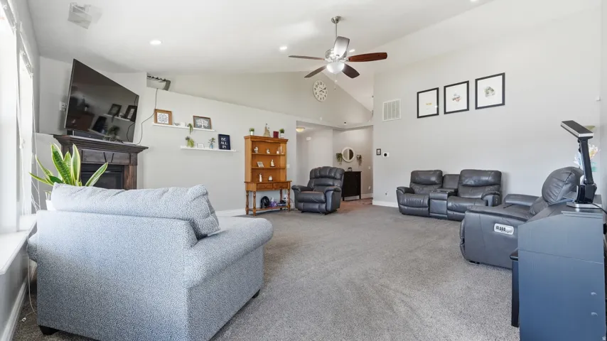 Vaulted ceilings, a built-in fireplace with a dark wood mantel, recessed lighting, and a ceiling fan