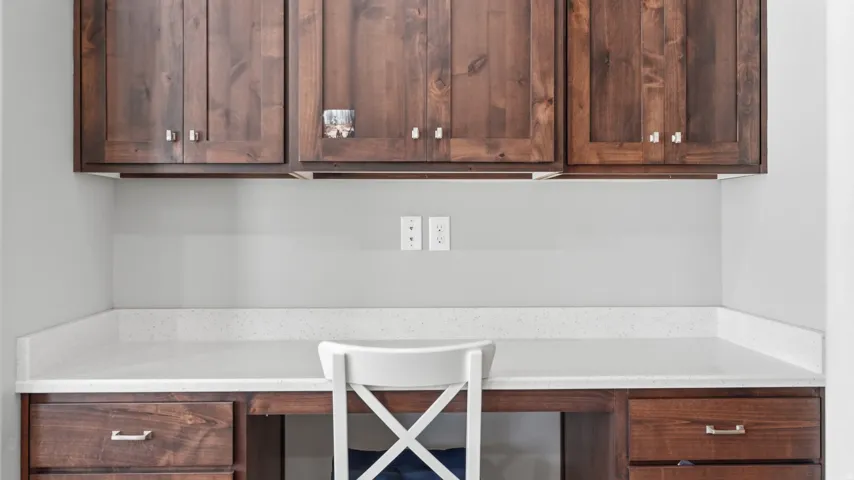Built-in desk with wood-finish cabinetry, light-toned countertop, and overhead storage