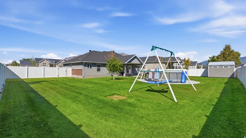 Expansive backyard with a manicured lawn, white privacy fencing, and a detached storage shed