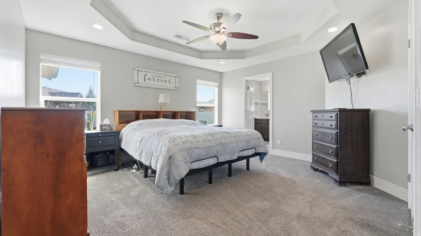 Tray ceiling with a ceiling fan, dual windows, and recessed lighting