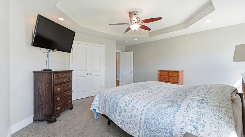 Tray ceiling with recessed lighting, ceiling fan with light fixture, light gray wall finish, and white paneled doors