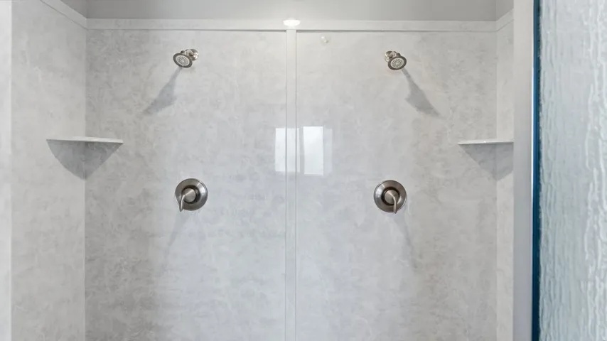 Dual shower heads with brushed nickel finishes, integrated wall shelving, and a clear glass enclosure