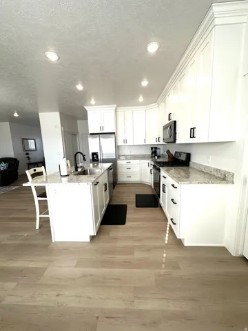 Kitchen featuring an island, white cabinetry, integrated appliances, recessed lighting, and light wood-finish flooring