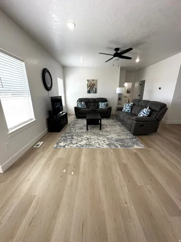 Spacious living area featuring light wood-finish flooring, recessed lighting, and a ceiling fan