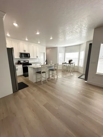 Kitchen featuring recessed lighting, white cabinetry, a center island with bar seating, stainless steel appliances, and wood-finish flooring