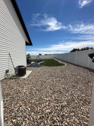 Expansive backyard with a white privacy fence, ornamental gravel, and a manicured lawn