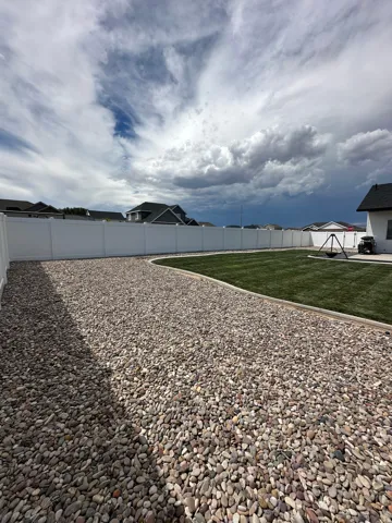 Expansive backyard featuring a manicured lawn, gravel landscaping, and a perimeter privacy fence