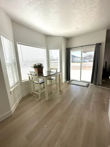 Light wood-finish flooring, white walls, multiple windows with blinds, and a sliding glass door