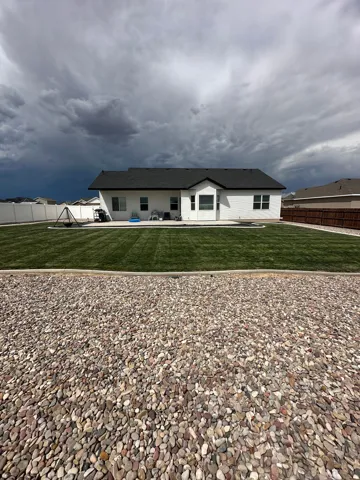 Expansive backyard featuring a manicured lawn, white vinyl fencing, and a concrete patio