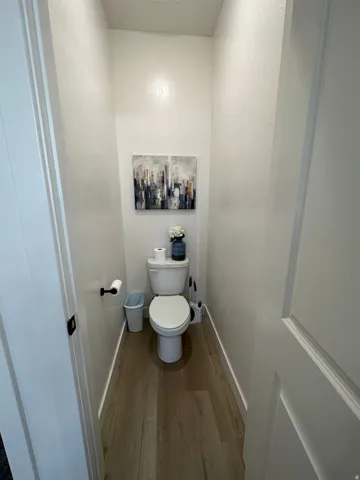 Wood-finish flooring with white baseboards and a ceramic toilet