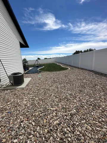 Spacious backyard with a white privacy fence, river rock landscaping, and a manicured lawn area