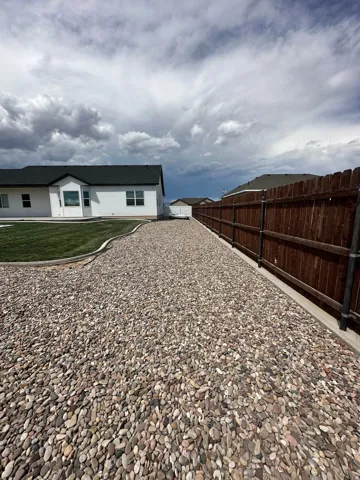 Gravel pathway extending alongside a privacy fence and a white-sided residence with a dark roof