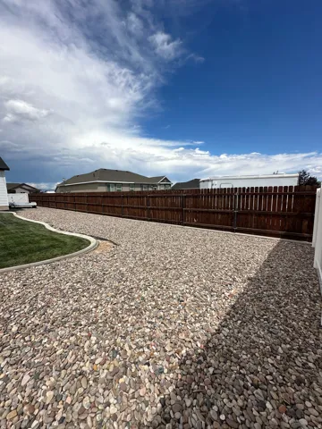 Gravel hardscaping, manicured lawn, dark wood privacy fencing, and white vinyl fencing