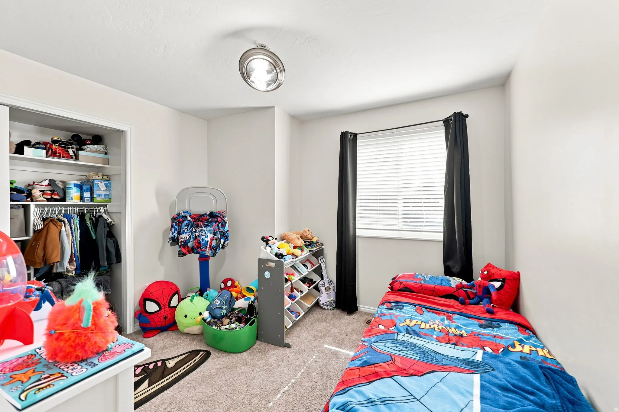 White walls, ceiling-mounted light fixture, carpeted flooring, window with blinds, and a built-in closet with shelving and hanging space