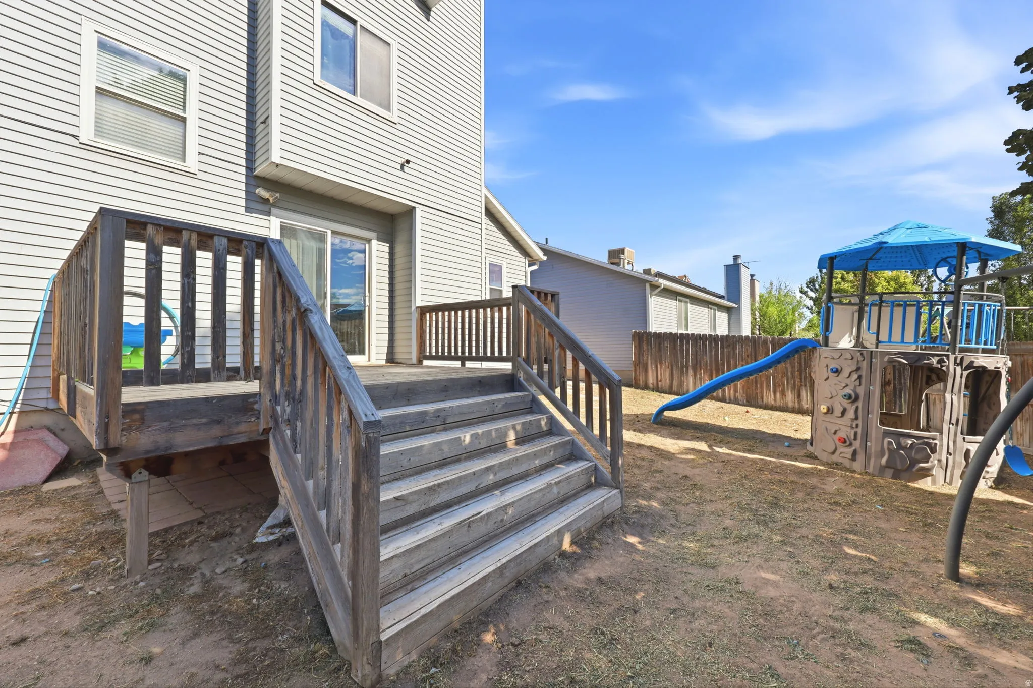 Exterior siding with multiple windows, wooden deck with stairs, and sliding glass door