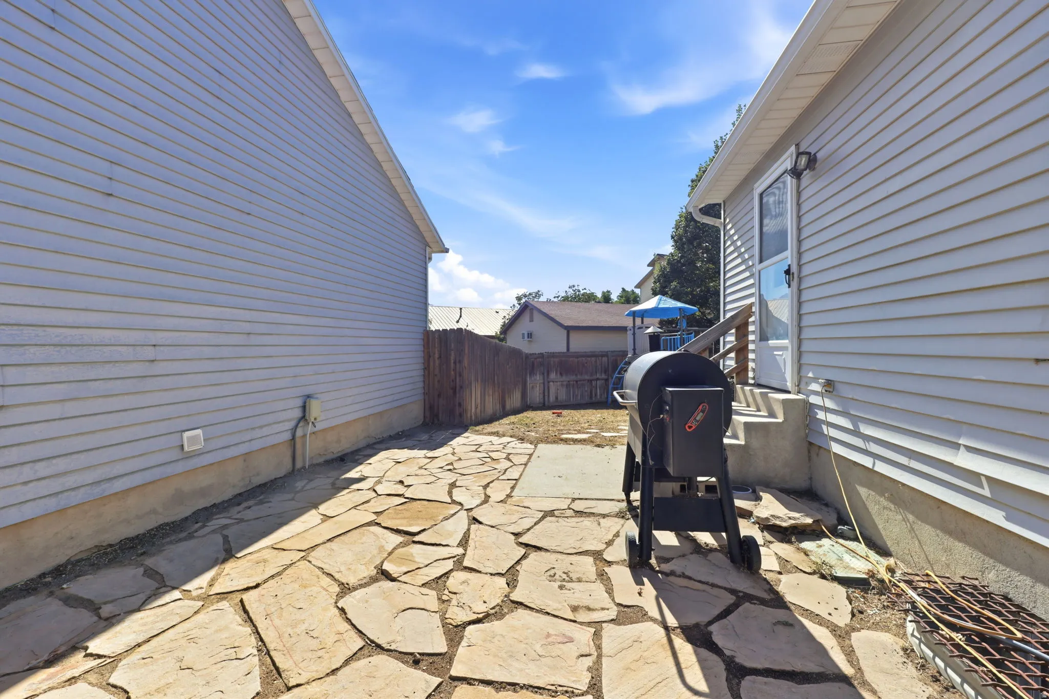 Flagstone patio surface, vinyl siding exterior, wood fence perimeter, exterior lighting fixture, concrete steps
