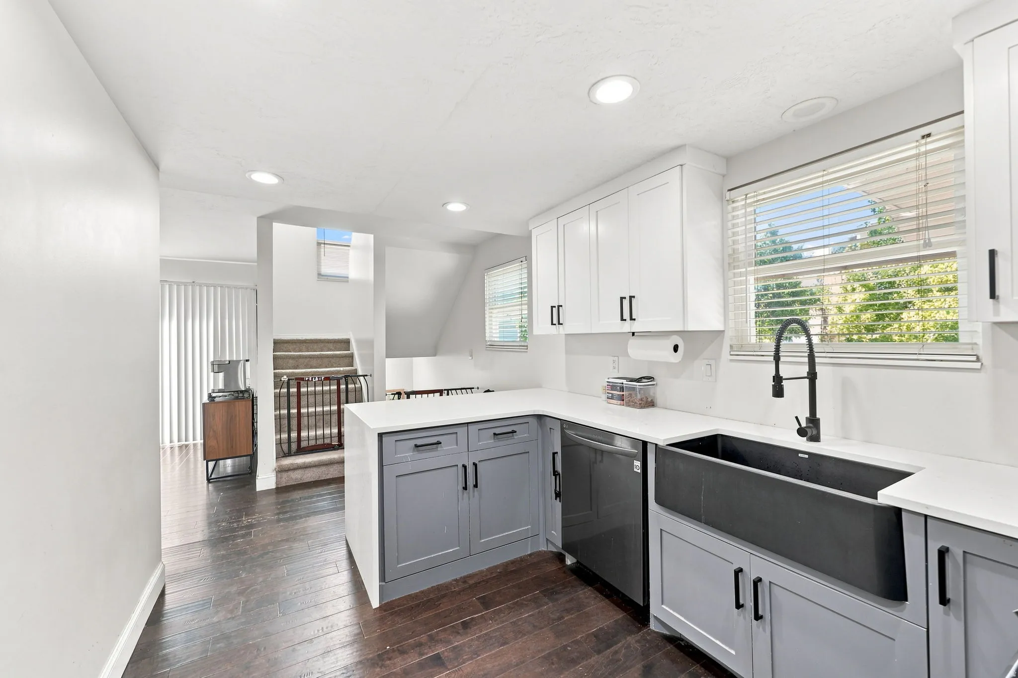 Modern kitchen featuring white upper cabinetry, gray lower cabinetry, a dark farmhouse sink, quartz countertops, and dark wood-finish flooring