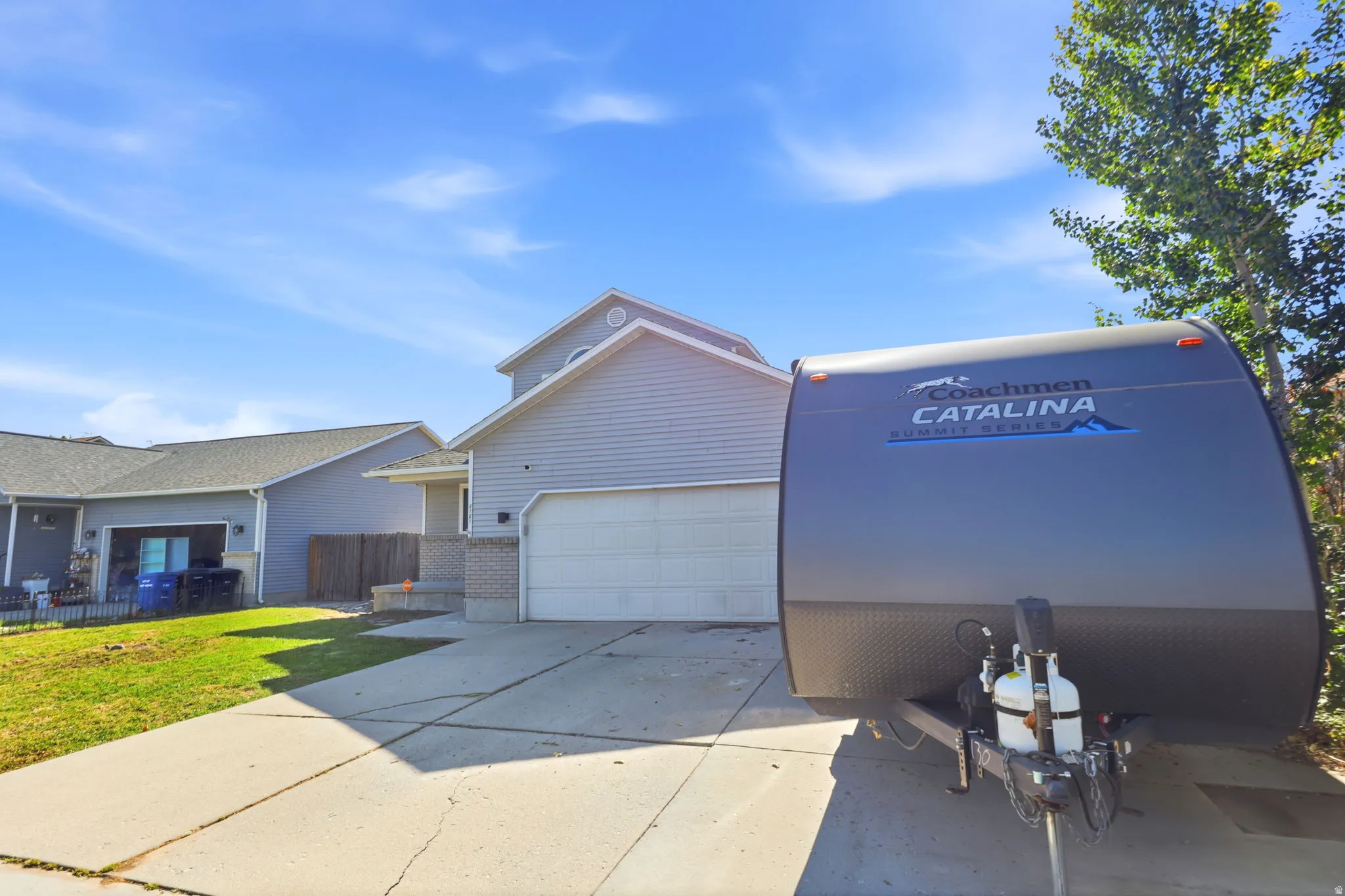Two-story residential structure with light gray siding and a white garage door, featuring a concrete driveway and an adjacent grassy area