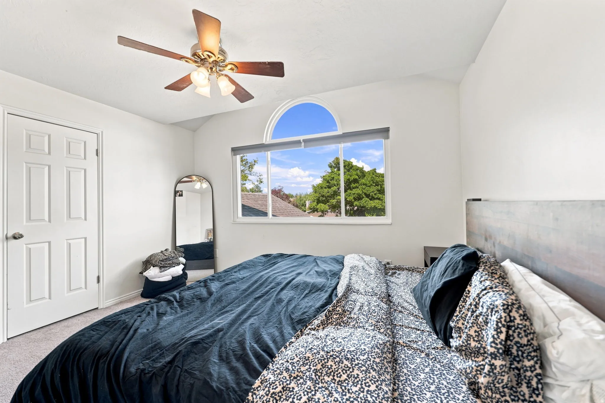 Vaulted ceiling with a ceiling fan, arched window accent, and neutral-toned wall paint