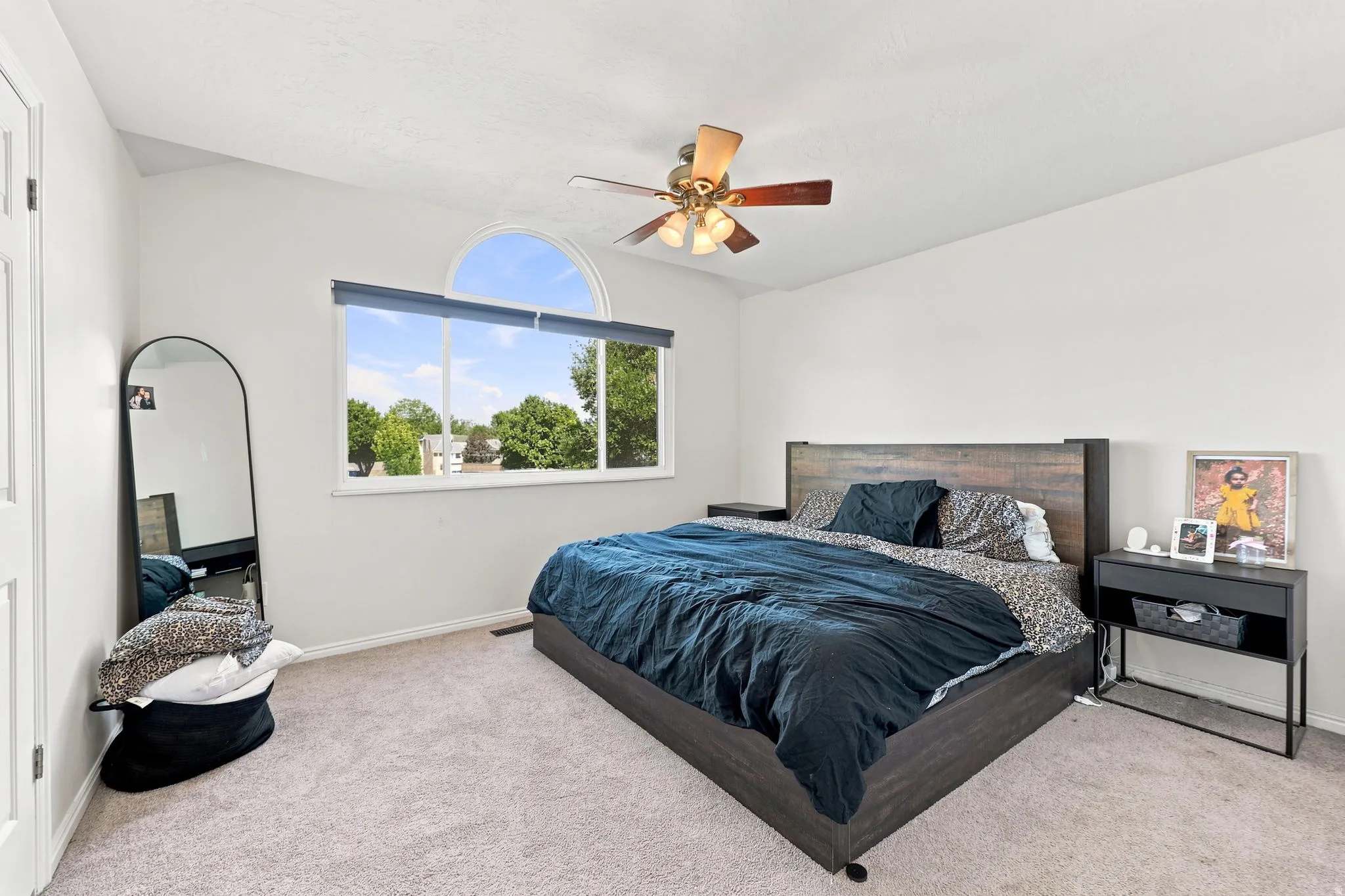 Carpeted room with a vaulted ceiling, ceiling fan, and a large window with an arched transom