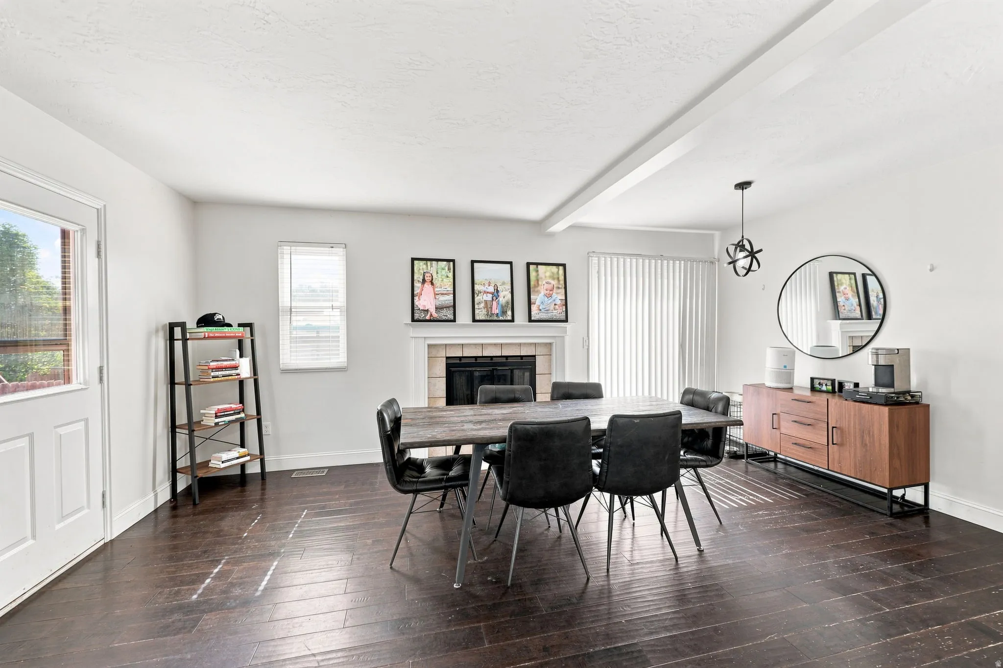 Dark wood-finish flooring, white walls, built-in fireplace with mantel, white ceiling beams, and a sliding glass door