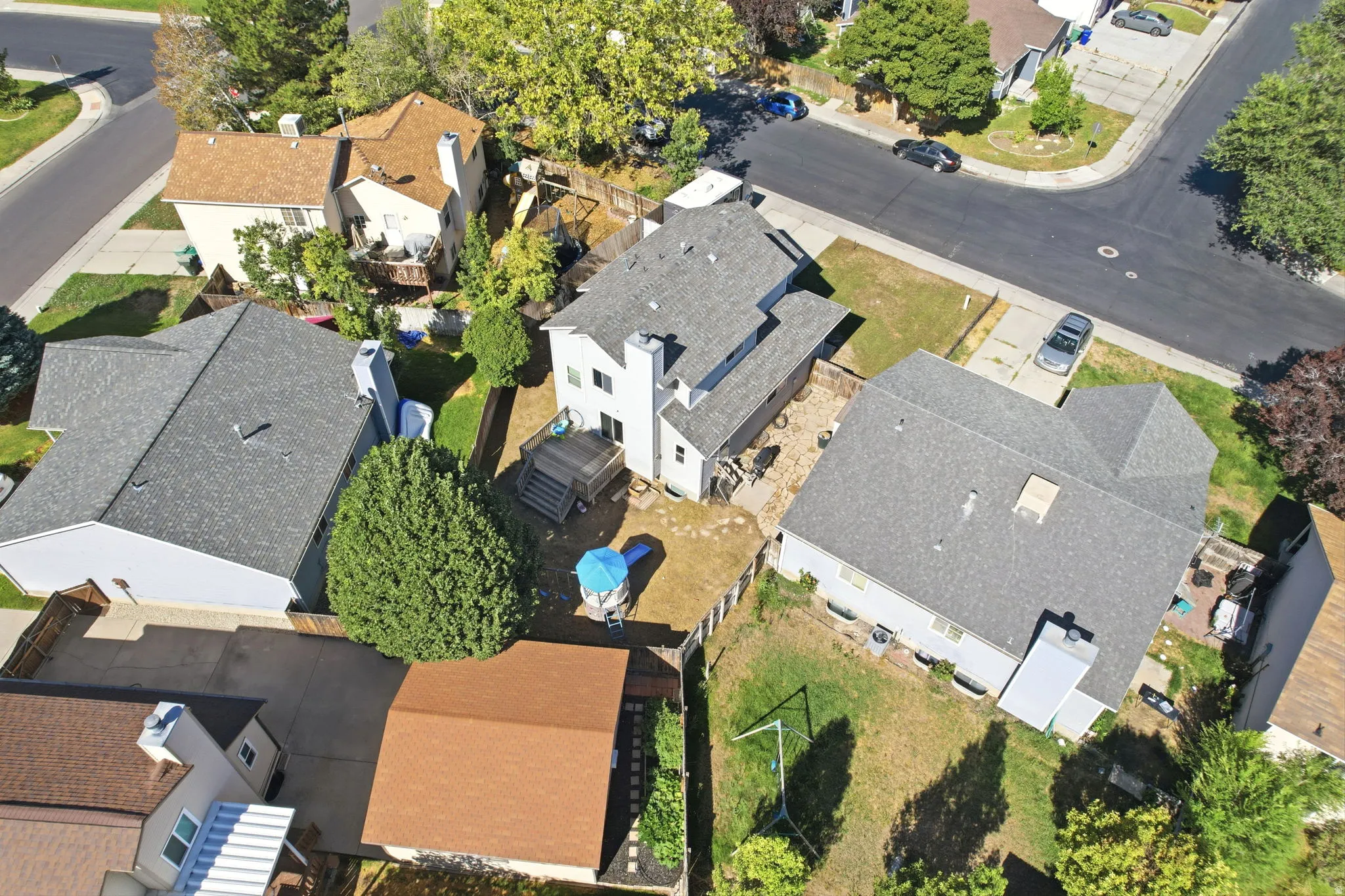 Asphalt shingle roof, paved driveway, concrete patio, wood fencing, mature trees