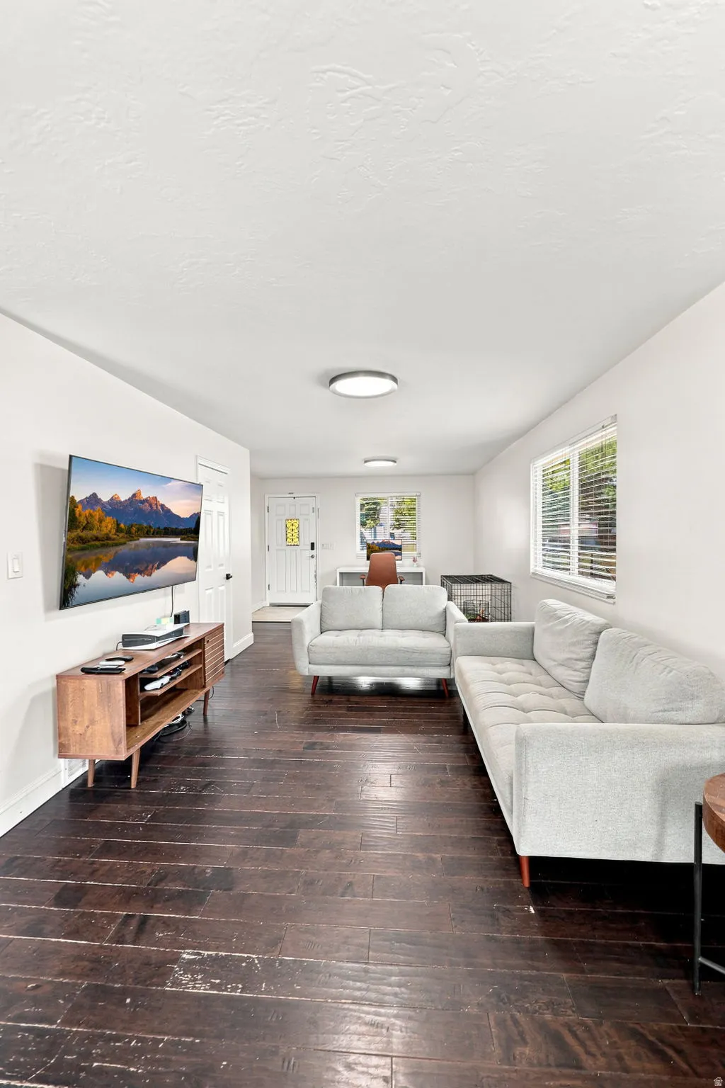 Dark wood-finish flooring throughout, white walls, and multiple windows with blinds