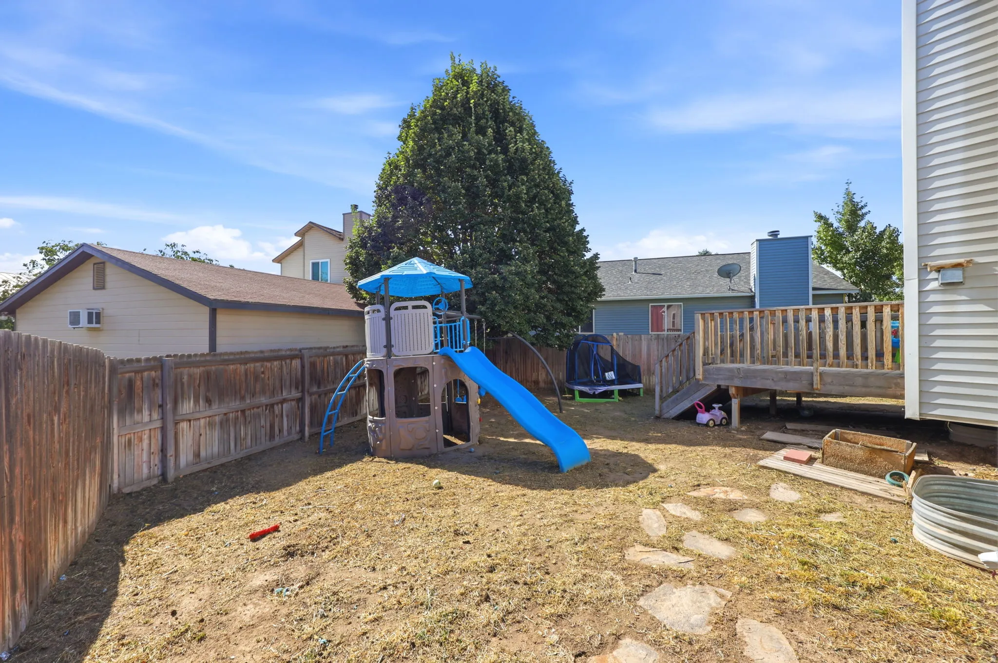 Expansive backyard with a wooden fence, elevated wood deck, and stone pathway