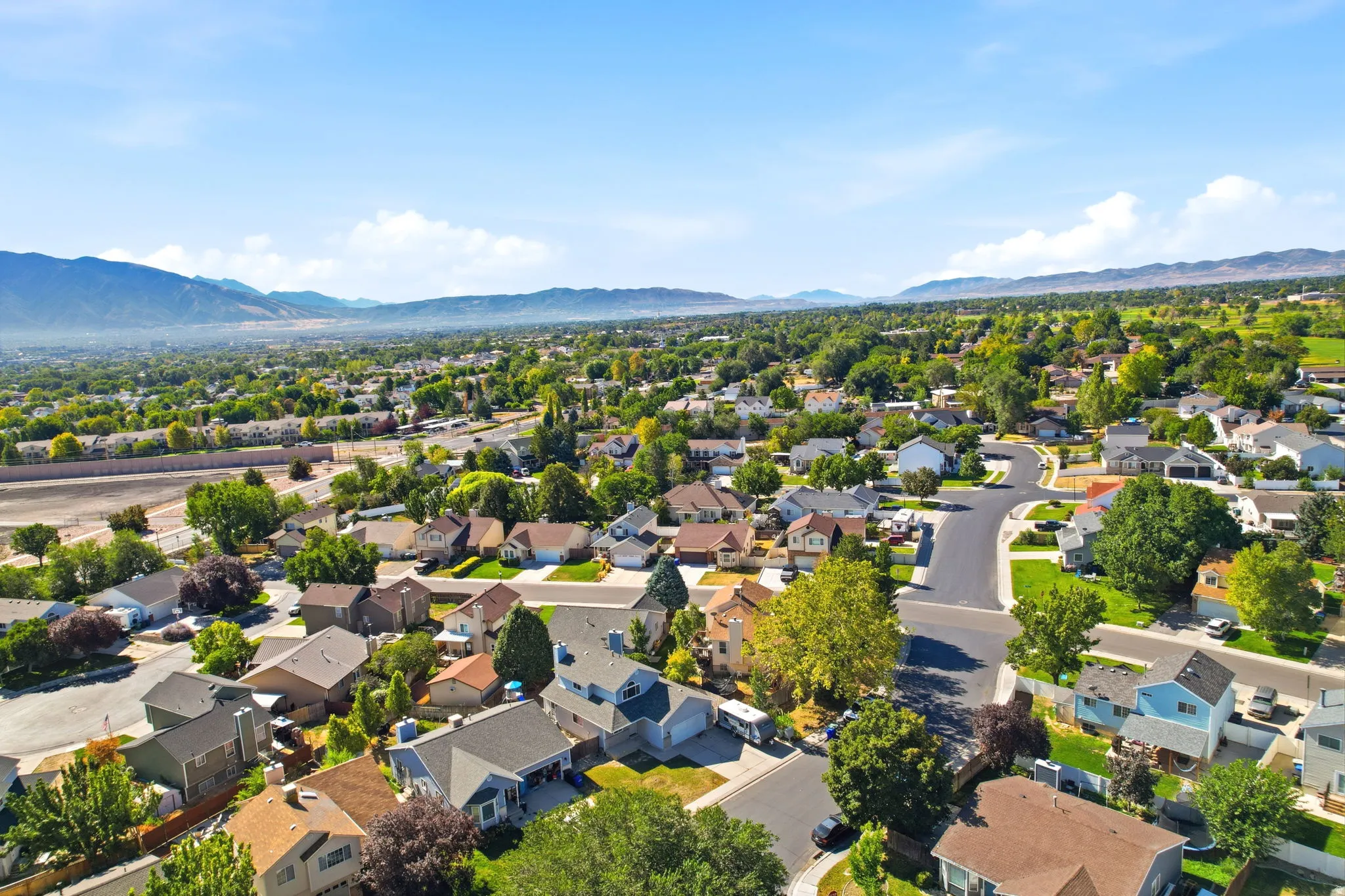 Expansive residential area with numerous detached properties, abundant mature trees, paved roadways, and distant mountain ranges