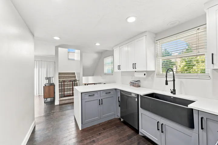 Modern kitchen featuring white upper cabinetry, gray lower cabinetry, a dark farmhouse sink, quartz countertops, and dark wood-finish flooring
