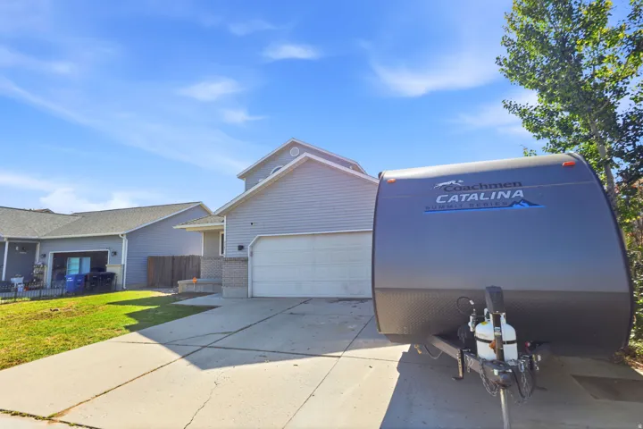 Two-story residential structure with light gray siding and a white garage door, featuring a concrete driveway and an adjacent grassy area