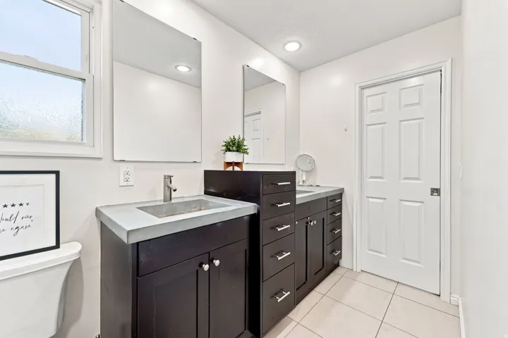 Dual vanity with integrated sinks, dark wood-finish cabinetry, and contemporary wall-mounted mirrors